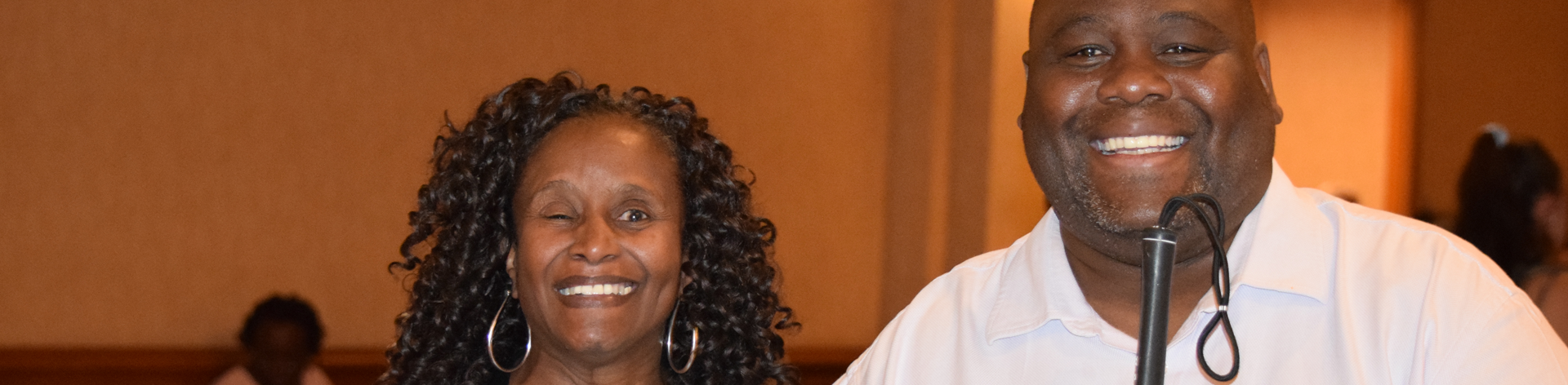 A blind man and woman smile for a photo together at a convention.